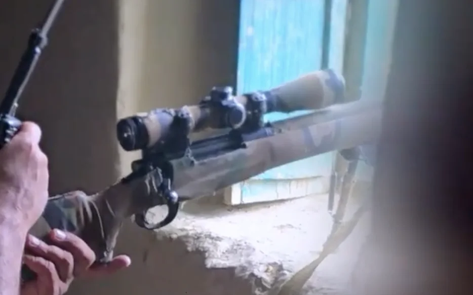 Frame at 05:05: Bolt-action rifle aimed through a window