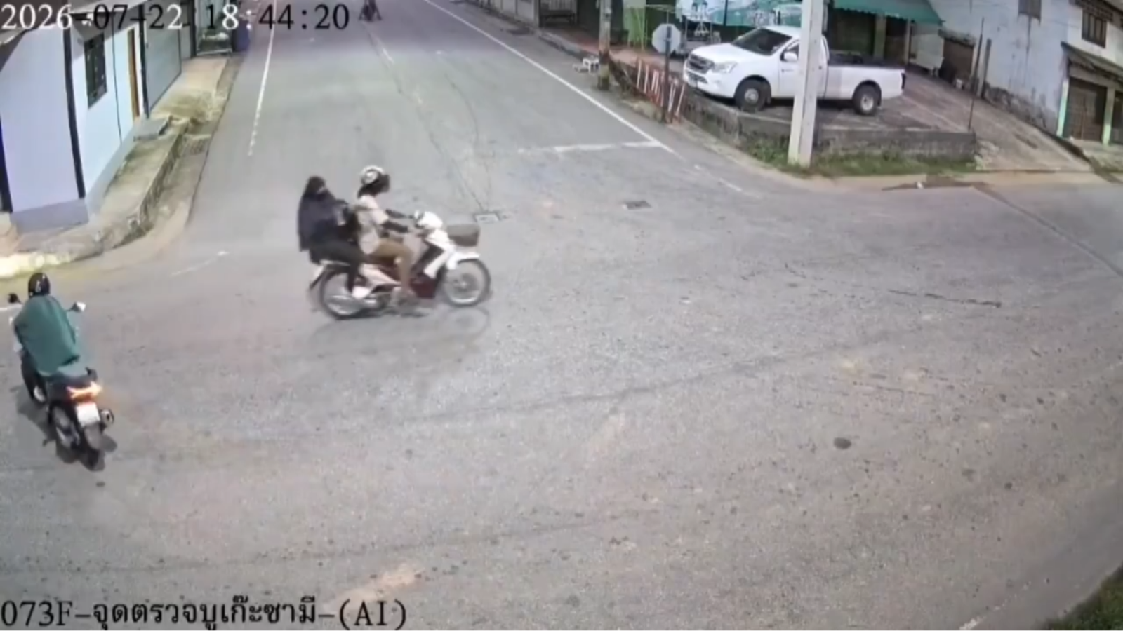 CCTV frame showing a red-and-white scooter carrying two riders arriving at a road intersection, with a bystander on another scooter at the left.