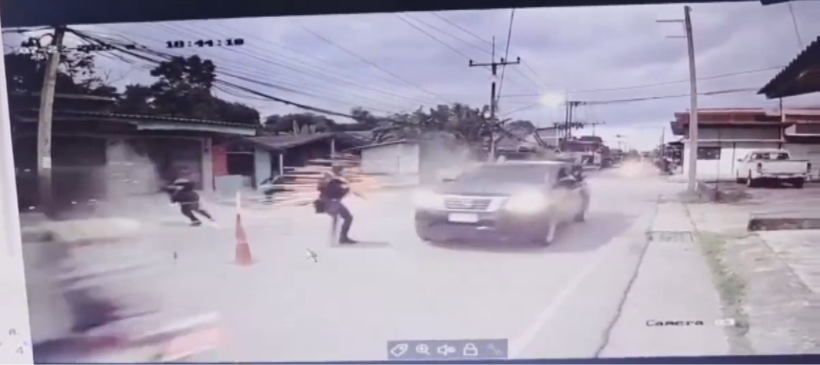 Low-resolution CCTV view along a street showing figures moving near a vehicle amid dust as the attack begins.