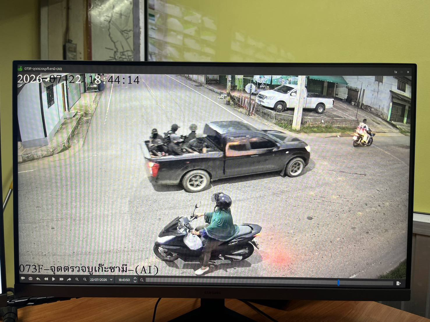 CCTV frame showing six masked men holding rifles in the bed of a black pickup truck passing a road junction, with two scooters nearby.